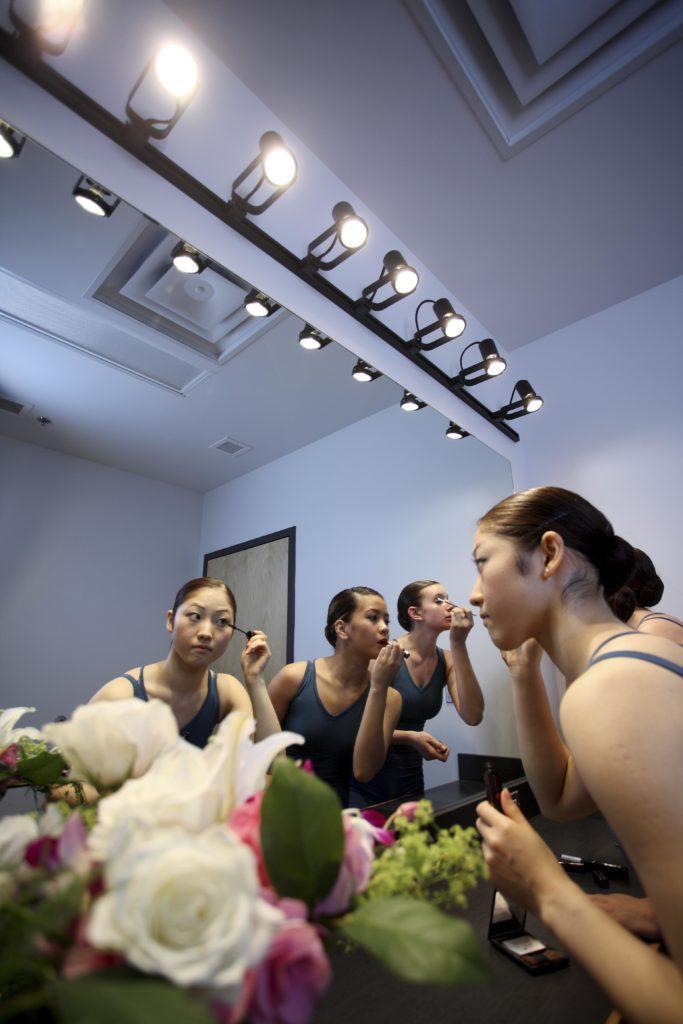 ballerinas standing in front of a dressing room mirror applying makeup